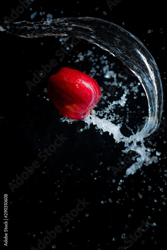 An apple floating in the air with water on a black background