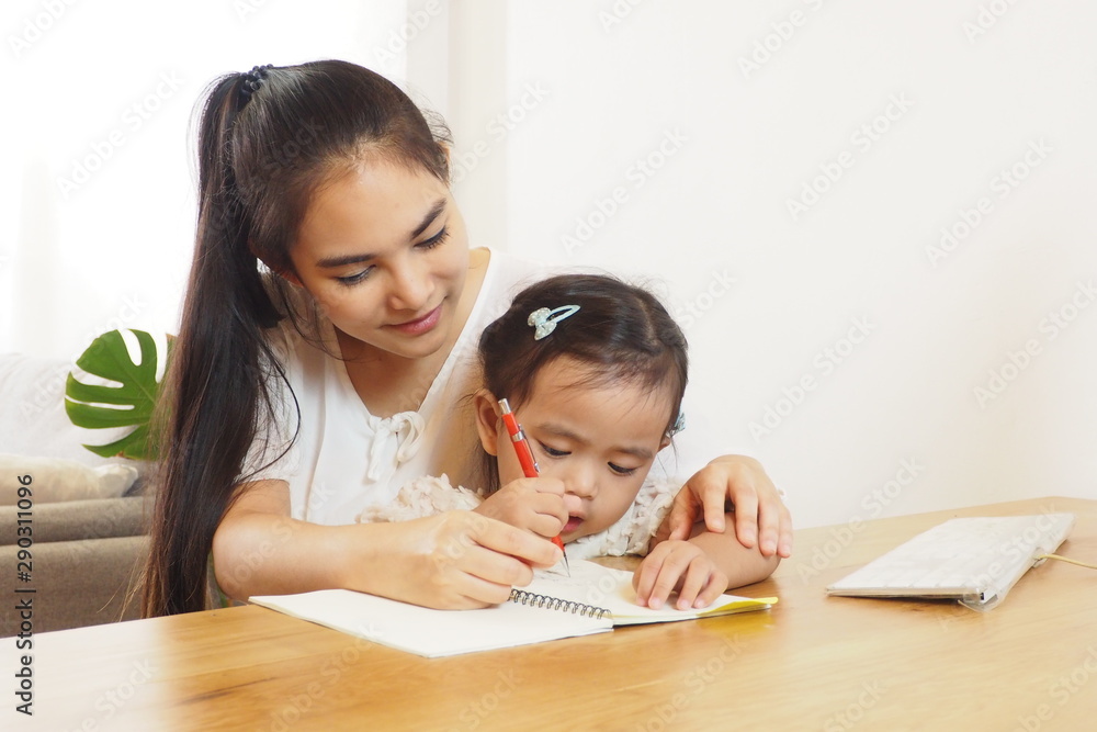 Warm moment of Asian mother helping and teaching her cute daughter doing homework on the table at home. Preschool kid learning, happy family, mother and daughter lifestyle and activity concept Warm moment of Asian mother helping and teaching her cute daughter doing homework on the table at home. Preschool kid learning, happy family, mother and daughter lifestyle and activity concept