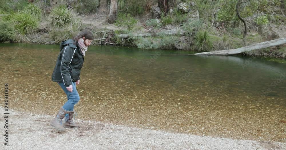 woman on a stony riverbank attempting to skip stones across the creek. woman throwing stones into a river, beautiful tranquil bush creek woman on a stony riverbank attempting to skip stones across the creek. woman throwing stones into a river, beautiful tranquil bush creek