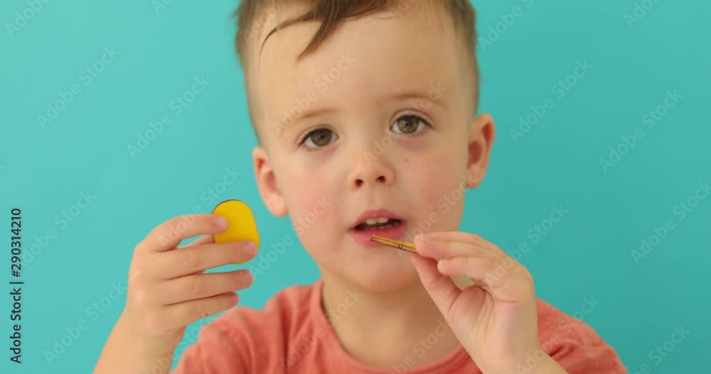 Adorable curios kid holding yellow oval and triangle and showing at camera on turquoise background Adorable curios kid holding yellow oval and triangle and showing at camera on turquoise background