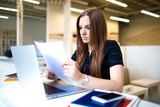 Business woman reading resume before interviews with employees using laptop computer for verification of information. Female economist exploring paper documents.Professional marketer reading summary