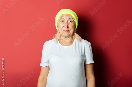 Funny old woman in a hat, makes a hand gesture on a pink background. Concept cool stylish grandmother, modern style