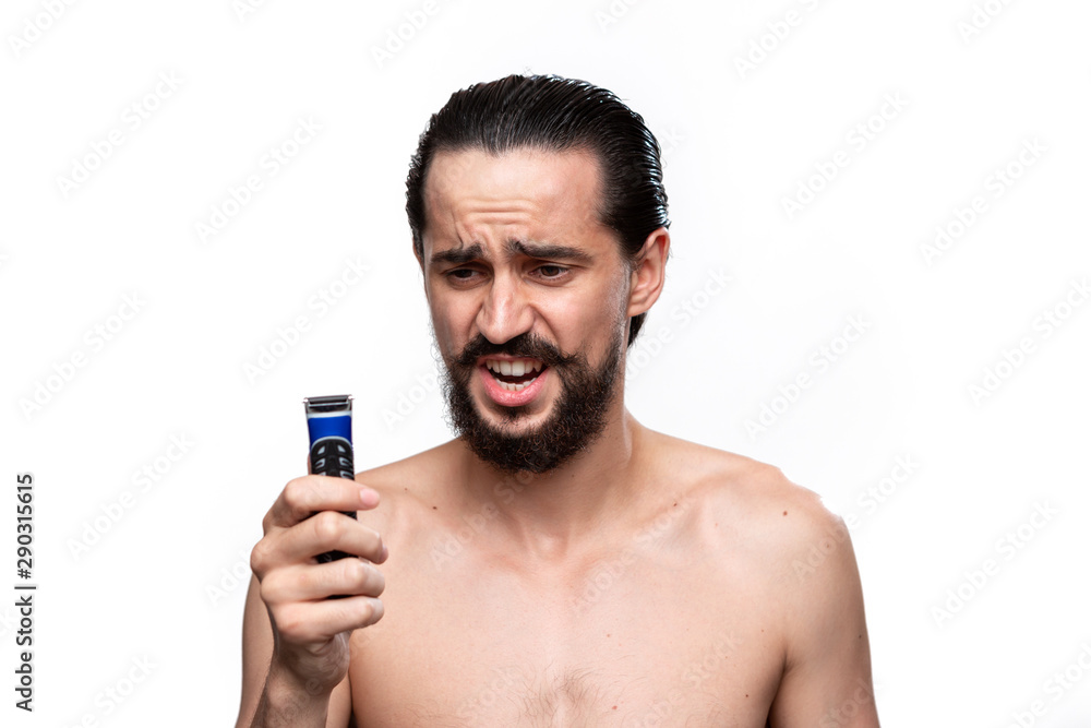 Fototapeta premium Excited bearded man with mustache holds electric shaver standning bare isolated over white background. Concept of morning treatment and shaving. Time to trim your beard.