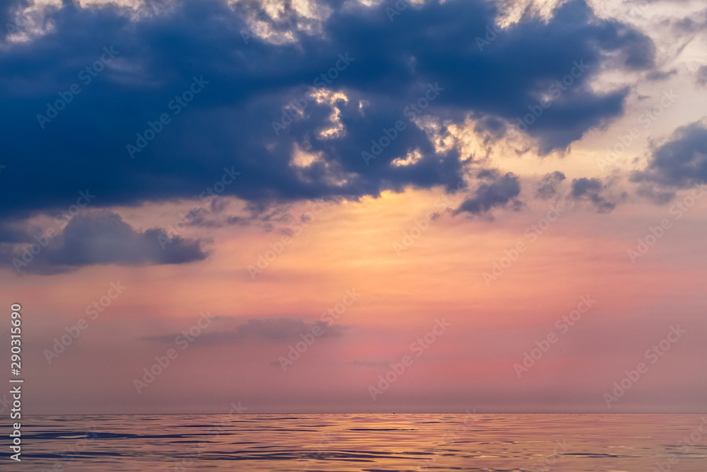 sunset in different colors of the sky, the sun behind the dark clouds, the calm sea water with its wonderful reflection of colors
