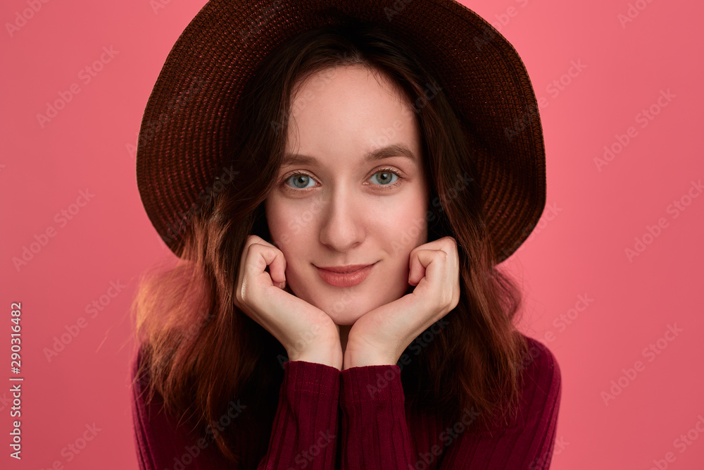 Close-up portrait of a happy beautiful brunette girl in a wide-brimmed hat posing on a dark pink background. Close-up portrait of a happy beautiful brunette girl in a wide-brimmed hat posing on a dark pink background.