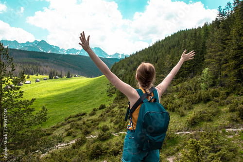 Woman tourist with hands in the air standing on a cliff of rock.