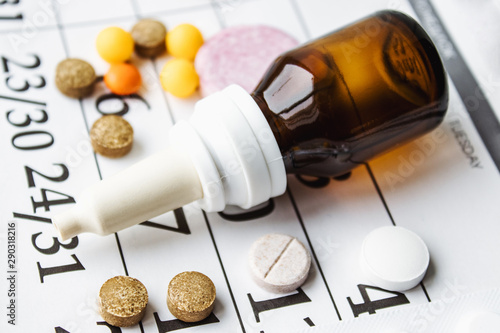 Pills, supplements and medicines for the disease. A pile of various pills and a bottle of therapeutic drops in a bottle on a calendar background.