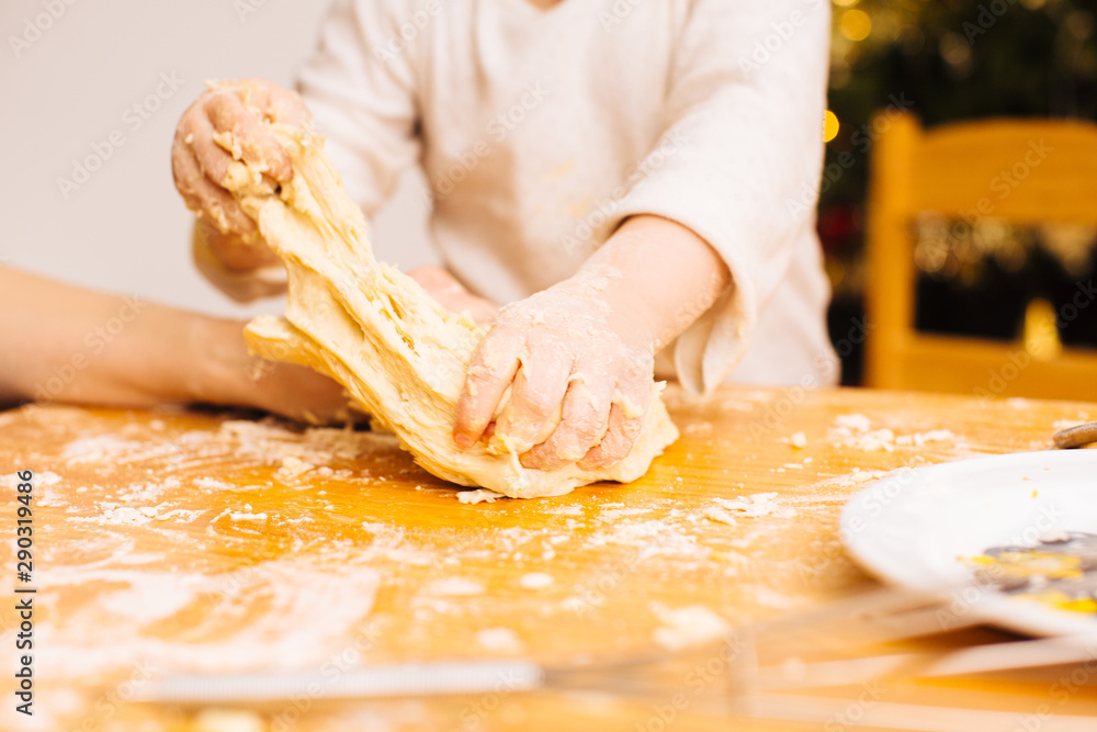 Detail of toddler  hands kneading  and stretching dough on wooden table