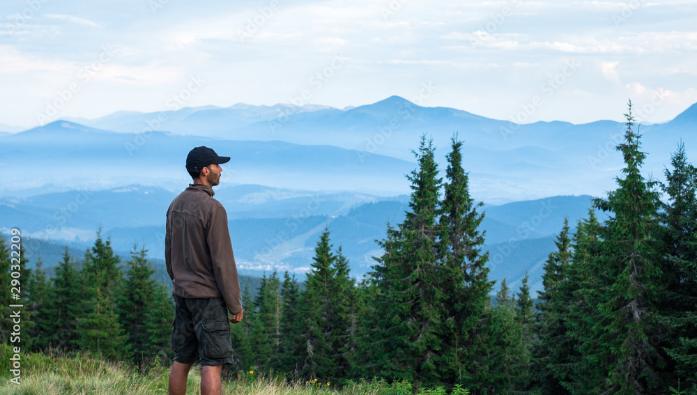 hiker man in cap admires the scenery of mountain range covered with blue fog in carpathian mountains hiker man in cap admires the scenery of mountain range covered with blue fog in carpathian mountains