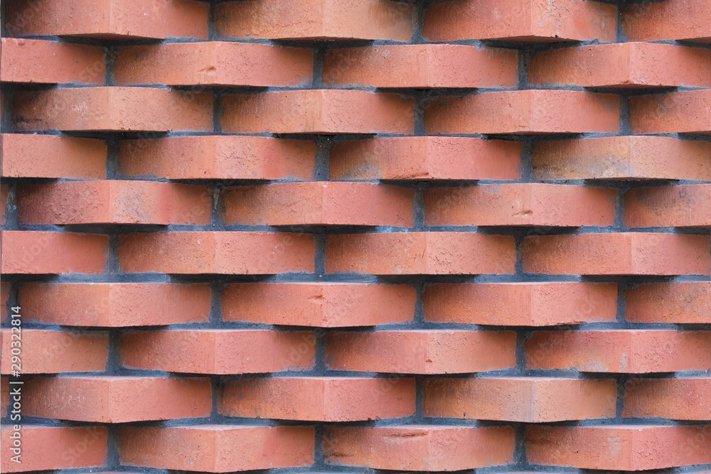 A wall of red brick laid in horizontal rows. The corners of the bricks stick outward forming a volumetric surface pattern