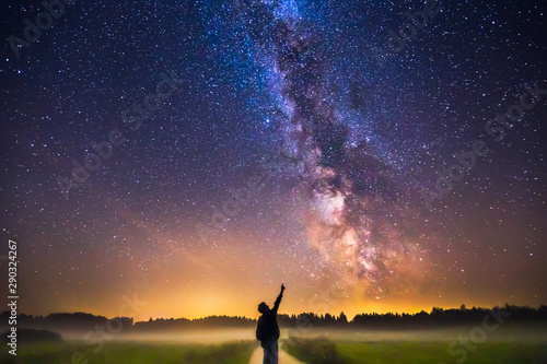 Landscape with Milky way galaxy and man silhuette pointing to the stars photo