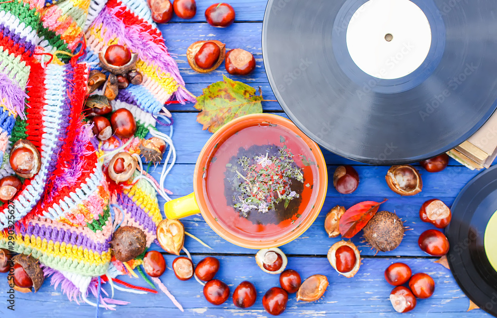 Yellow ceramic cup of herbal tea and vintage vinyl records on aged wooden background with fall autumn leaves and chestnuts.