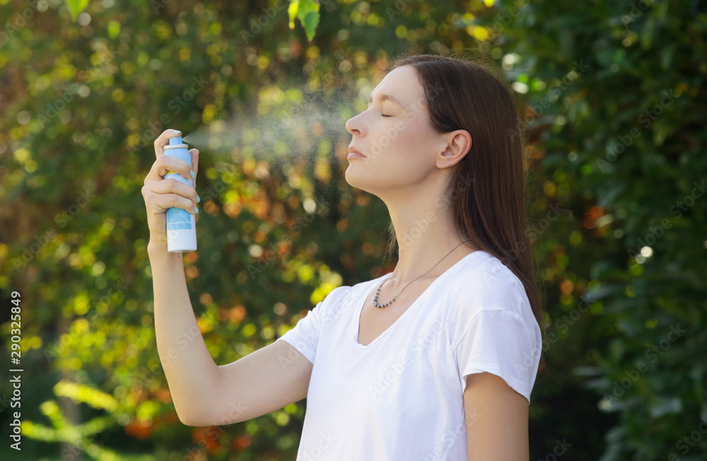 Woman spraying facial mist on her face, summertime skincare concept Woman spraying facial mist on her face, summertime skincare concept
