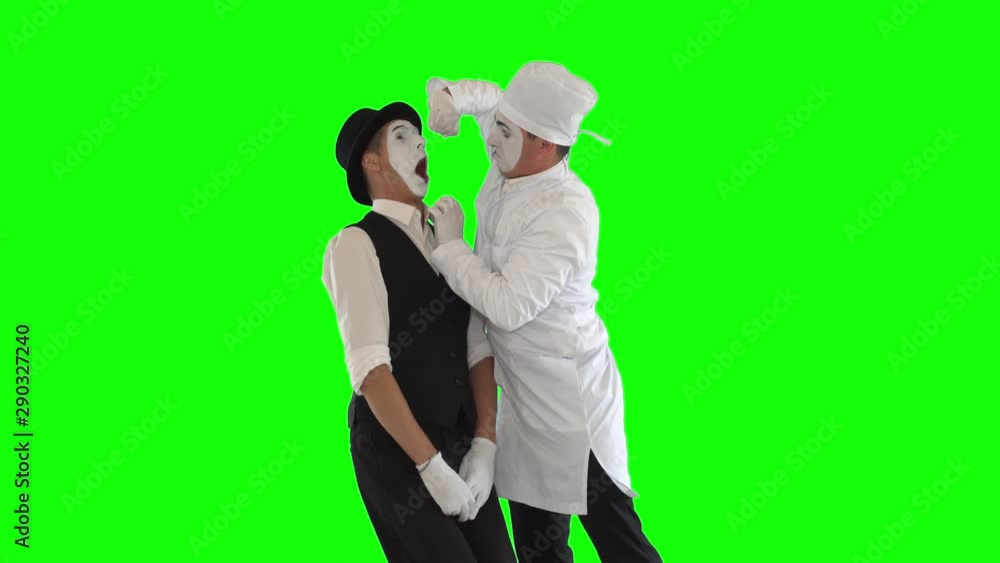 Funny male mime in white gown and imitating work of evil dentist. The patient afraids of the doctor. Two actors making show on green background. Chromakey Funny male mime in white gown and imitating work of evil dentist. The patient afraids of the doctor. Two actors making show on green background. Chromakey