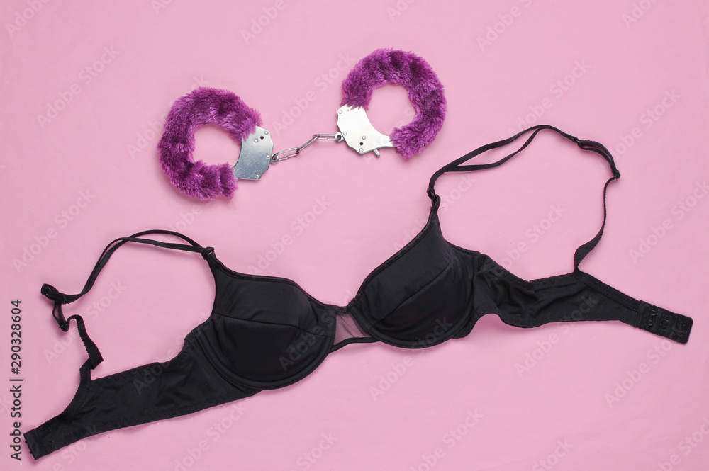 Handcuffs for sex games and black bra on pink background. Sexual bdsm toy. Fetish, erotic concept. Top view Handcuffs for sex games and black bra on pink background. Sexual bdsm toy. Fetish, erotic concept. Top view