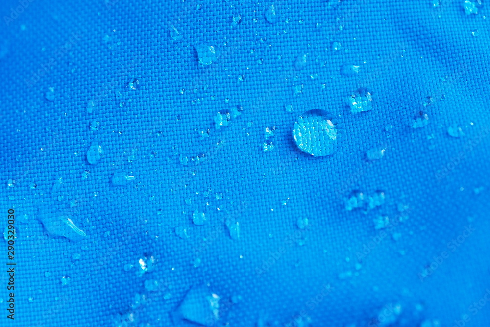 Closeup of water drops on bright blue fabric with waterproof design to protect fabric of the cloth from humidity and to offer easy cleaning to users. Fabric texture with design and background concept