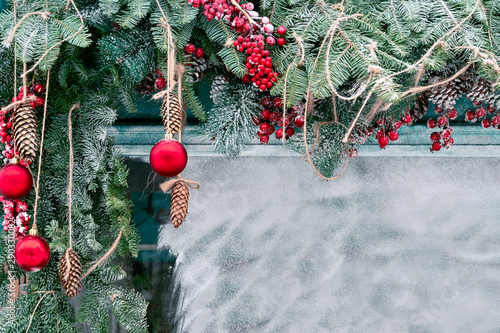 A view of a snowy window decorated with fir branches, red berries and balls, a rope, fir cones and pine cones. photo