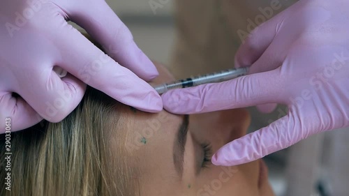 The doctor injects a facelift on a middle-aged woman on the forehead between the eyebrows to remove facial wrinkles in the room of the surgical clinic photo