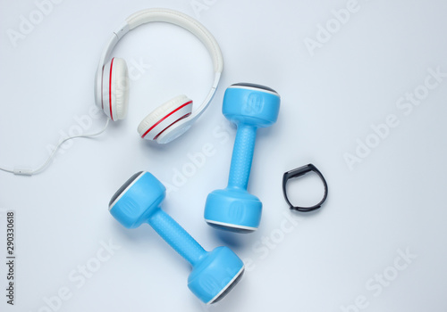 Dumbbells, smart bracelet, headphones on a white background. Minimalistic sport concept. Top view.