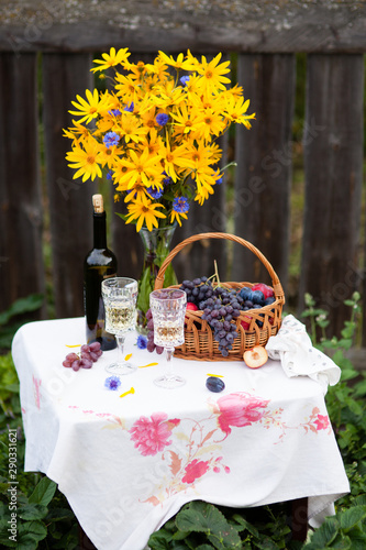bouquet of flowers, wine, glasses and grapes against the background of an old fence
