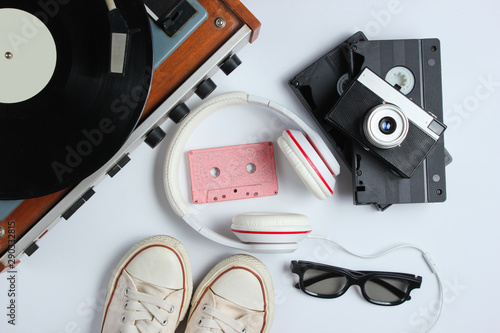 Flat lay retro 80s pop culture objects. Vinyl player, headphones, audio cassette, video tapes, film camera, sneakers on white background. Top view