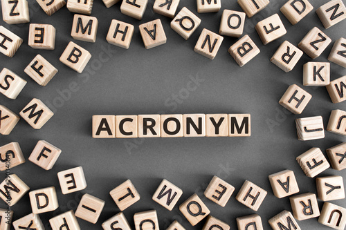 acronym - word from wooden blocks with letters, use of acronyms in the modern world abbreviation concept, random letters around, top view on wooden background photo