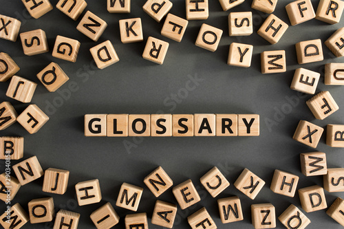 Glossary - word from wooden blocks with letters, alphabetical list with words meanings dictionary glossary  concept, random letters around, top view on grey background photo