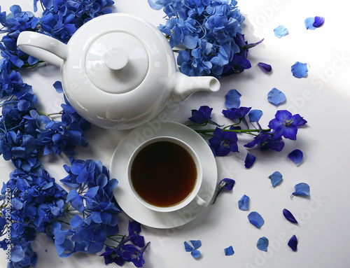 weiße Teetasse mit schwarzem Tee und weiße Teekanne mit blauen Blütenblättern photo