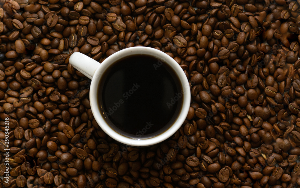 In coffee beans there is a white cup with coffee. Concept - morning coffee. Pleasure. In coffee beans there is a white cup with coffee. Concept - morning coffee. Pleasure.