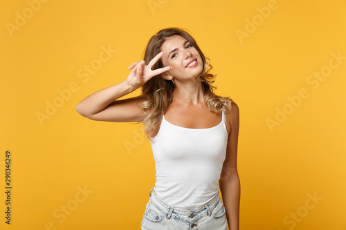 Beautiful young woman in light casual clothes posing isolated on yellow orange wall background, studio portrait. People sincere emotions lifestyle concept. Mock up copy space. Showing victory sign.