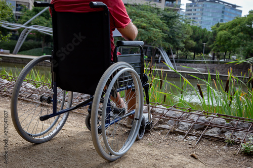 disabled man in wheelchair having fun while resting looking a tablet computer at park, concept of technological and occupational integration of people with disabilities and reduced mobility problems