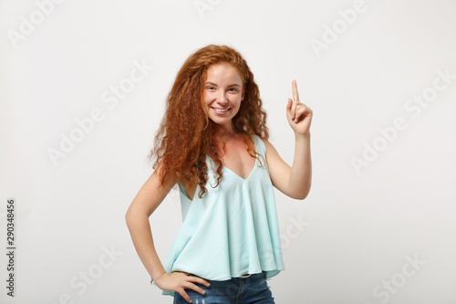 Young stunning redhead woman in casual light clothes posing isolated on white wall background studio portrait. People sincere emotions lifestyle concept. Mock up copy space. Pointing index finger up.