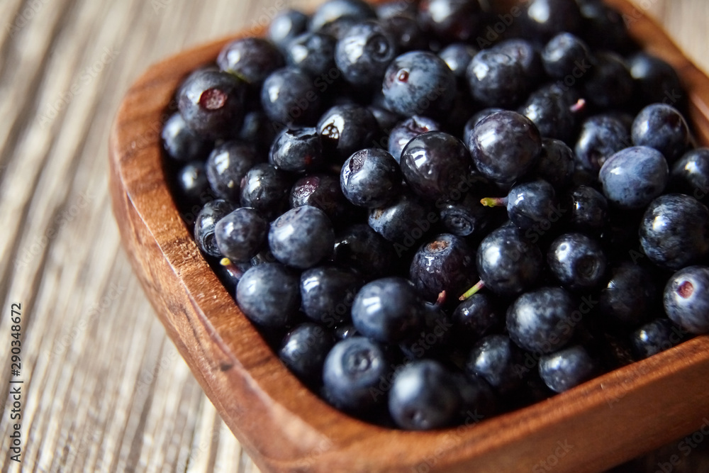 Bilberries closeup in a bowl on brown wooden background. Fresh dark berries on table