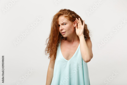 Young curious redhead woman girl in casual light clothes posing isolated on white wall background. People sincere emotions lifestyle concept. Mock up copy space. Try to hear you with hand near ear.