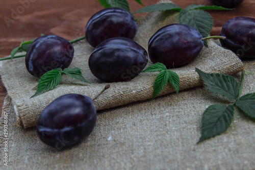 Fruits, plums purple, lying on a wooden kitchen table on a linen vintage napkin with green leaves of blackberries and raspberries