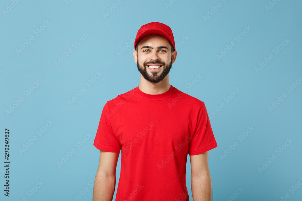 Delivery man in red uniform workwear isolated on blue wall background, studio portrait. Professional male employee in cap t-shirt print working as courier dealer. Service concept. Mock up copy space. - obrazy, fototapety, plakaty 