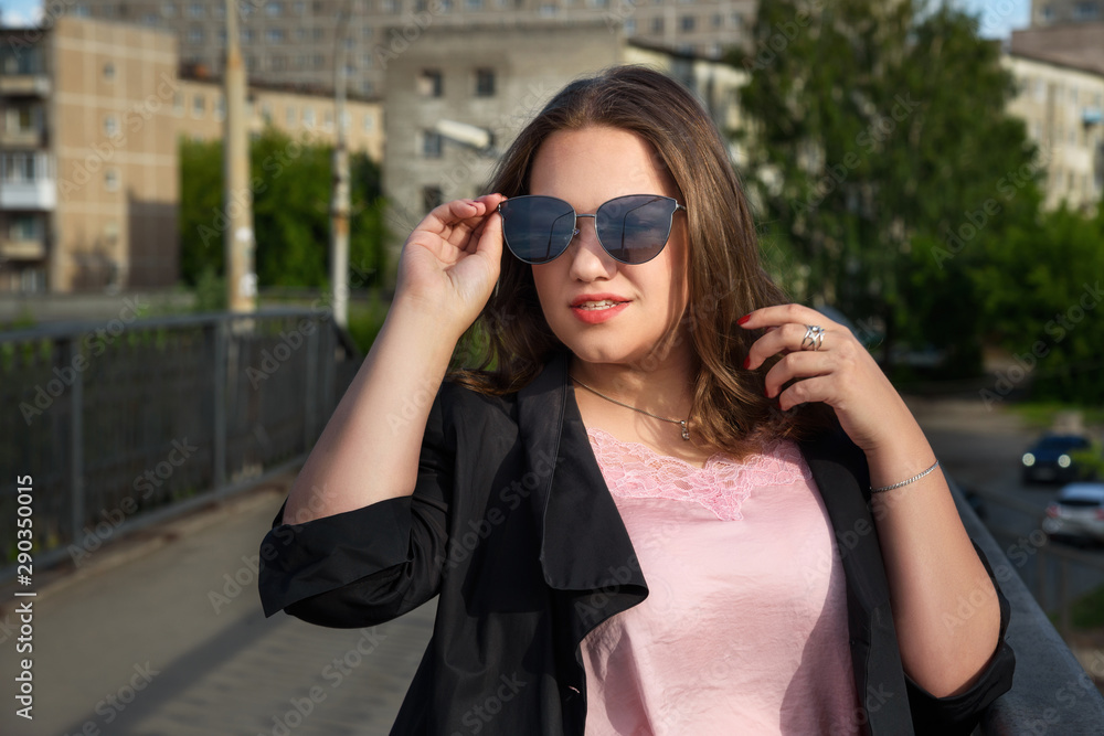 Brunette girl walking on the bridge in city. Girl in black jacket and red skirt with long hair. Plus size model Brunette girl walking on the bridge in city. Girl in black jacket and red skirt with long hair. Plus size model
