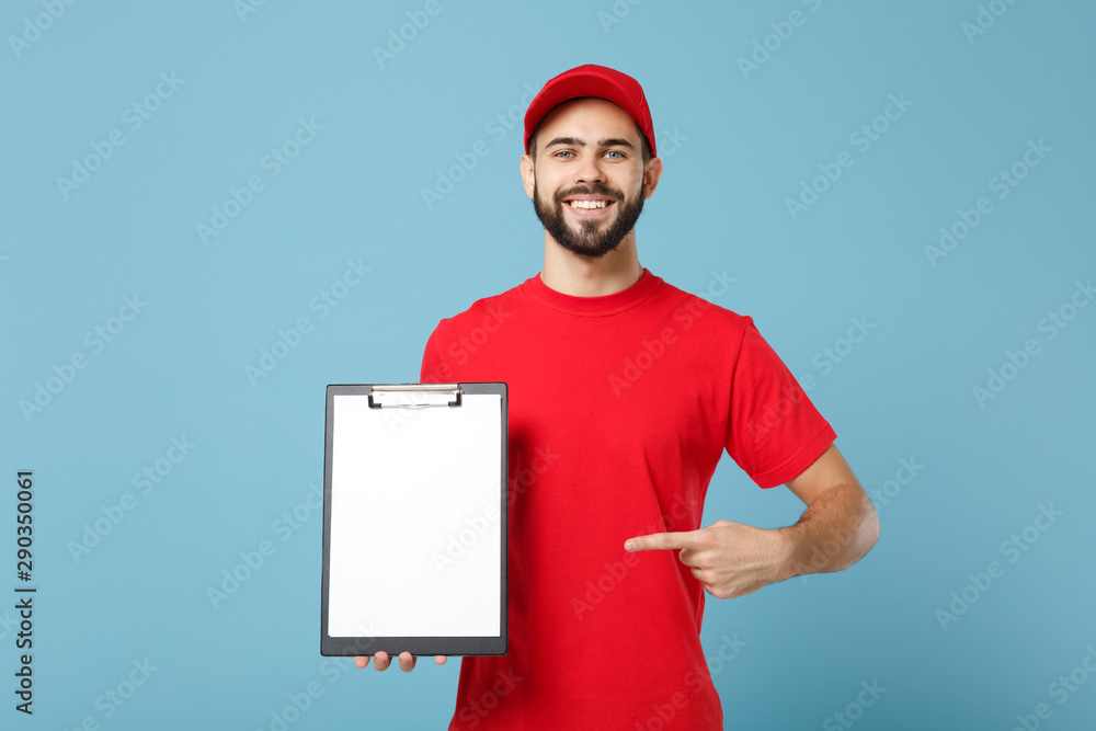 Delivery man in red uniform isolated on blue background, studio portrait. Professional male employee in cap t-shirt print working as courier dealer hold clipboard. Service concept. Mock up copy space.