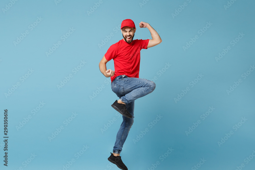 Delivery man in red uniform workwear isolated on blue wall background, studio portrait. Professional male employee in cap t-shirt print working as courier dealer. Service concept. Mock up copy space. Delivery man in red uniform workwear isolated on blue wall background, studio portrait. Professional male employee in cap t-shirt print working as courier dealer. Service concept. Mock up copy space.