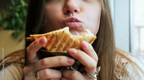 Billede på lærred Close-up portrait of young hungry woman with pleasure eats crisp toast in a cafe