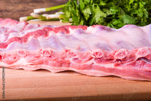 Fresh pork ribs on a wooden cutting board, fresh bunch of cilantro and green onions
