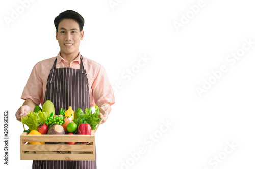 The Handsome young man asian 24s smile wearing brown apron and holding a wood basket of Non-Toxic fruits and vegetables without chemicals isolated on white background. 