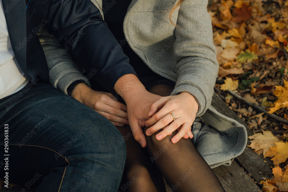 a pair of lovers in a coat sits on the ground in a pile of autumn leaves. A pair of people on the background of the autumn forest. a pair of lovers in a coat sits on the ground in a pile of autumn leaves. A pair of people on the background of the autumn forest.