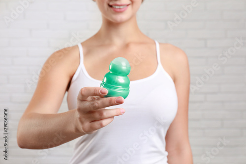 Young woman holding roll-on deodorant against brick wall, closeup