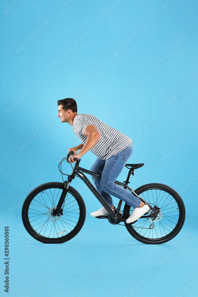 Handsome young man with modern bicycle on light blue background Handsome young man with modern bicycle on light blue background