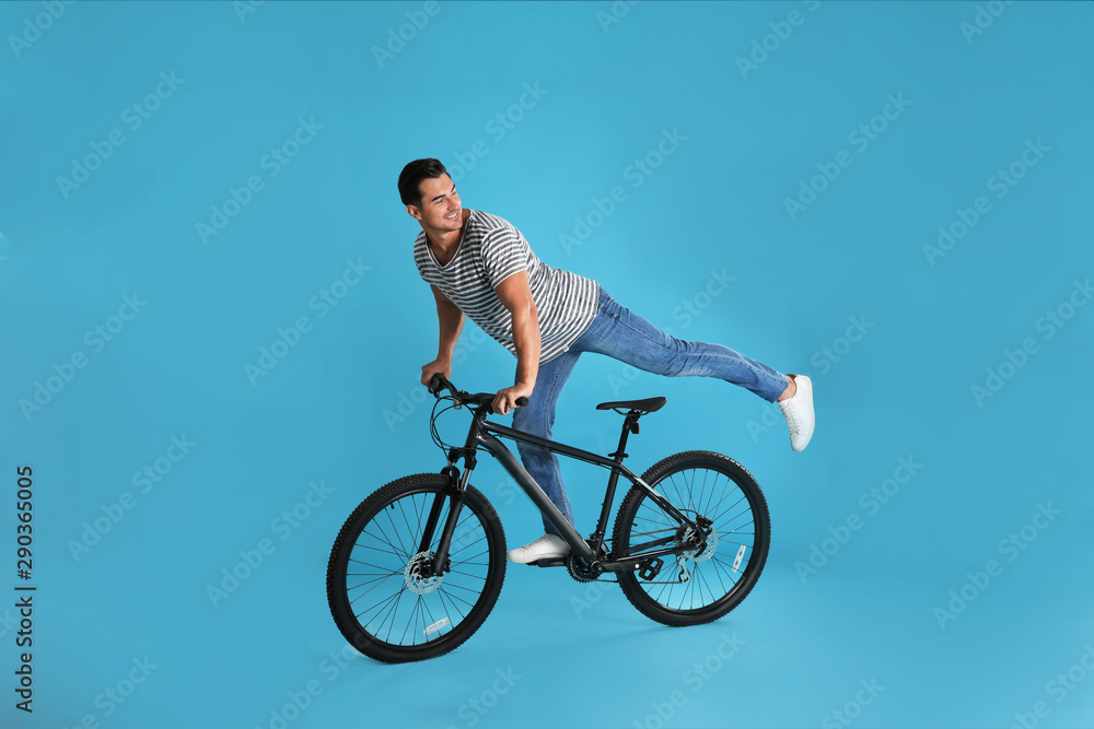 Handsome young man with modern bicycle on light blue background Handsome young man with modern bicycle on light blue background