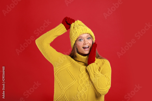 Emotional young woman in warm sweater, gloves and hat on red background. Winter season