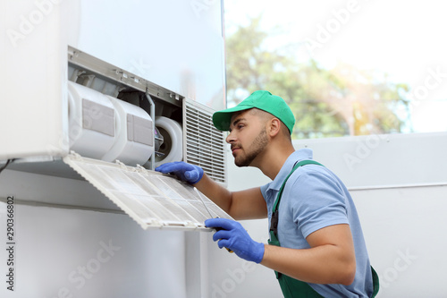 Professional technician maintaining modern air conditioner indoors