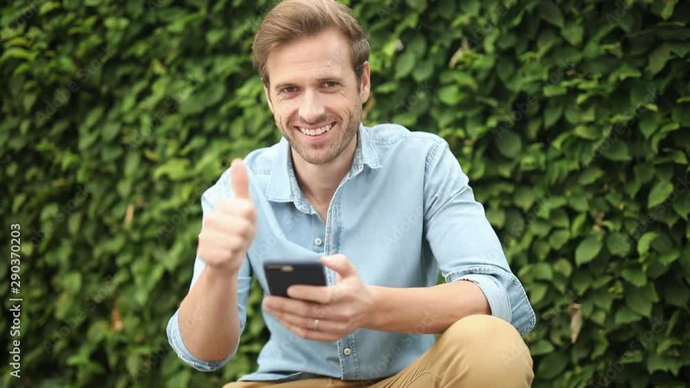 happy young man recommends what he read on his phone by making the ok thumbs up sign happy young man recommends what he read on his phone by making the ok thumbs up sign