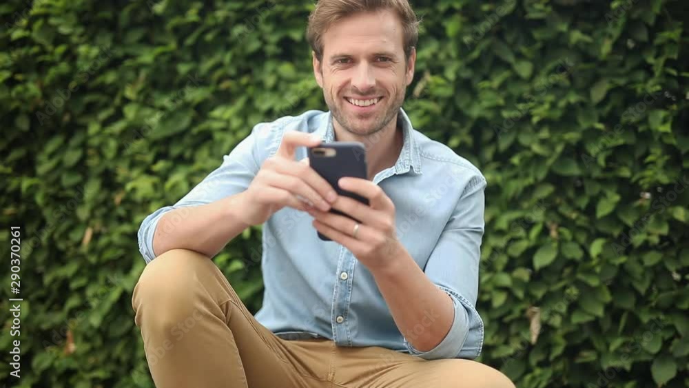 happy casual man standing down on sidewalk reads good news on the phone and makes ok sign happy casual man standing down on sidewalk reads good news on the phone and makes ok sign